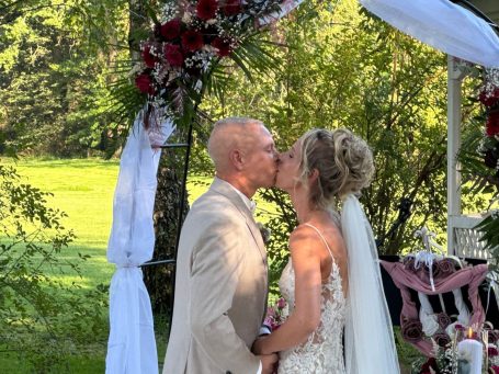 Braut und Bräutigam küssen sich unter einem Blumenbogen bei ihrer Hochzeit.