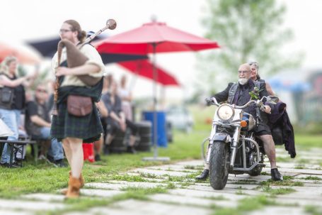 Ein Dudelsackspieler in traditioneller Kleidung, begleitet von einem Motorradfahrer.