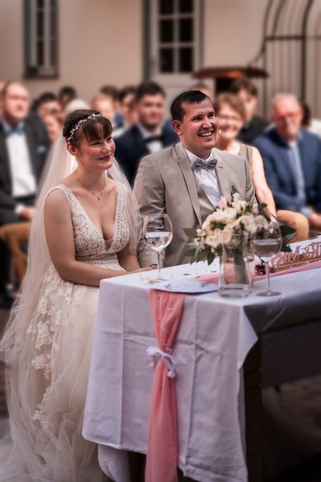 Braut und Bräutigam sitzen vor festlich gedecktem Tisch bei der Hochzeit.