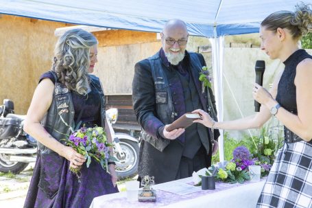 Brautpaar in Lederwesten, umgeben von Blumen, während einer Zeremonie unter einem Zelt.