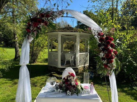 Eine romantische Gartendekoration mit Blumenbogen und Pavillon im Hintergrund.