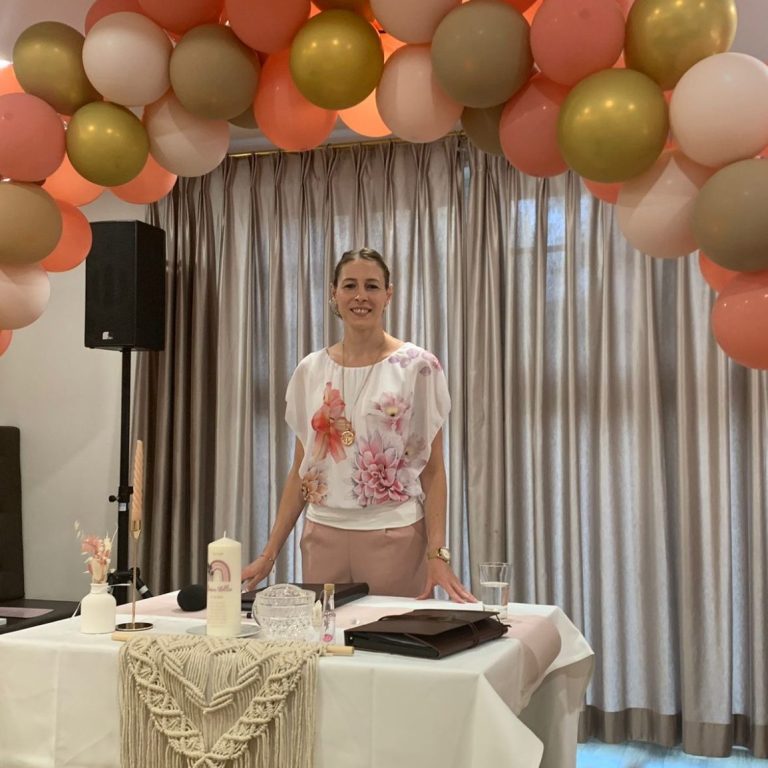 Frau steht an einem festlich dekorierten Tisch mit Ballons im Hintergrund.