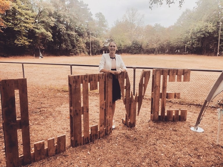 Frau steht neben großen Holzbuchstaben, die "LOVE" bilden, in einem parkähnlichen Umfeld.