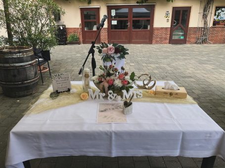 Tisch gedeckt mit Blumen, Dekorationen und einem Schild "Mr. & Mrs." im Freien.