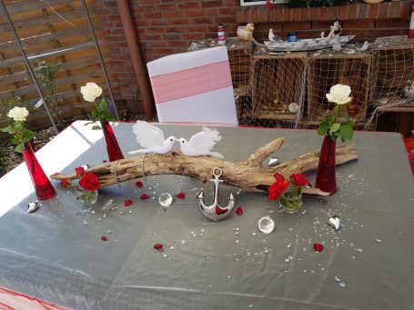 Tischdekoration mit Holzstück, roten und weißen Rosen in Vasen sowie Glitzer.