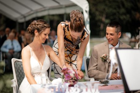 Braut und Bräutigam bei der Hochzeit, umgeben von Gästen und Feierlichkeiten.
